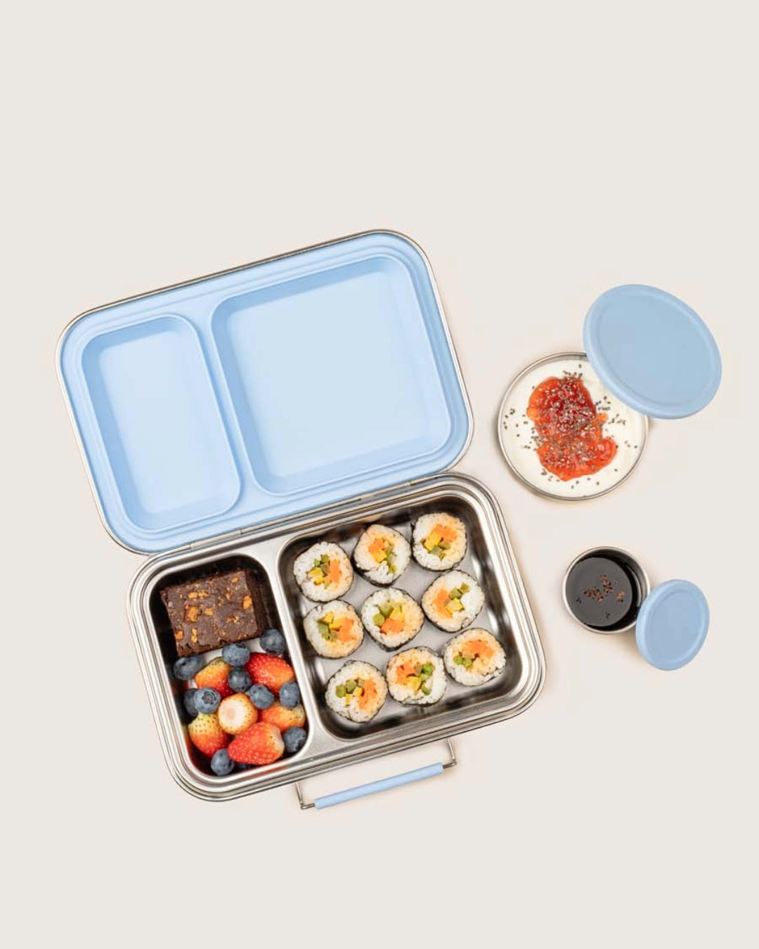 Baboons Bento Two Frost Blue leakproof stainless steel lunchbox with compartments containing sushi, fruits, healthy brownie and a small dish of sauce in matching snack boxes on a light background