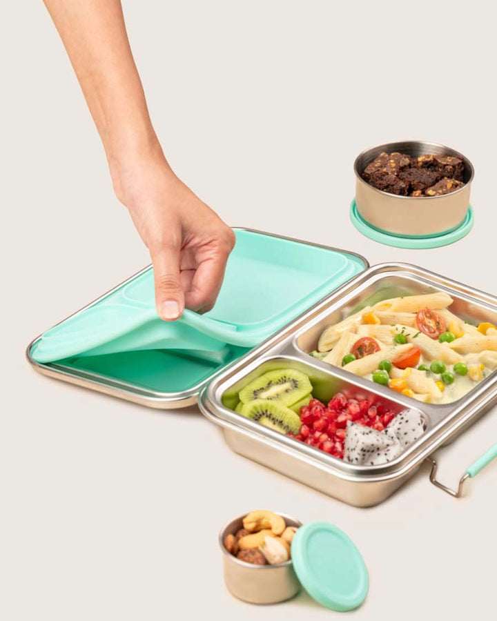 Stainless steel lunch box with compartments filled with food, including a hand opening the lid.
