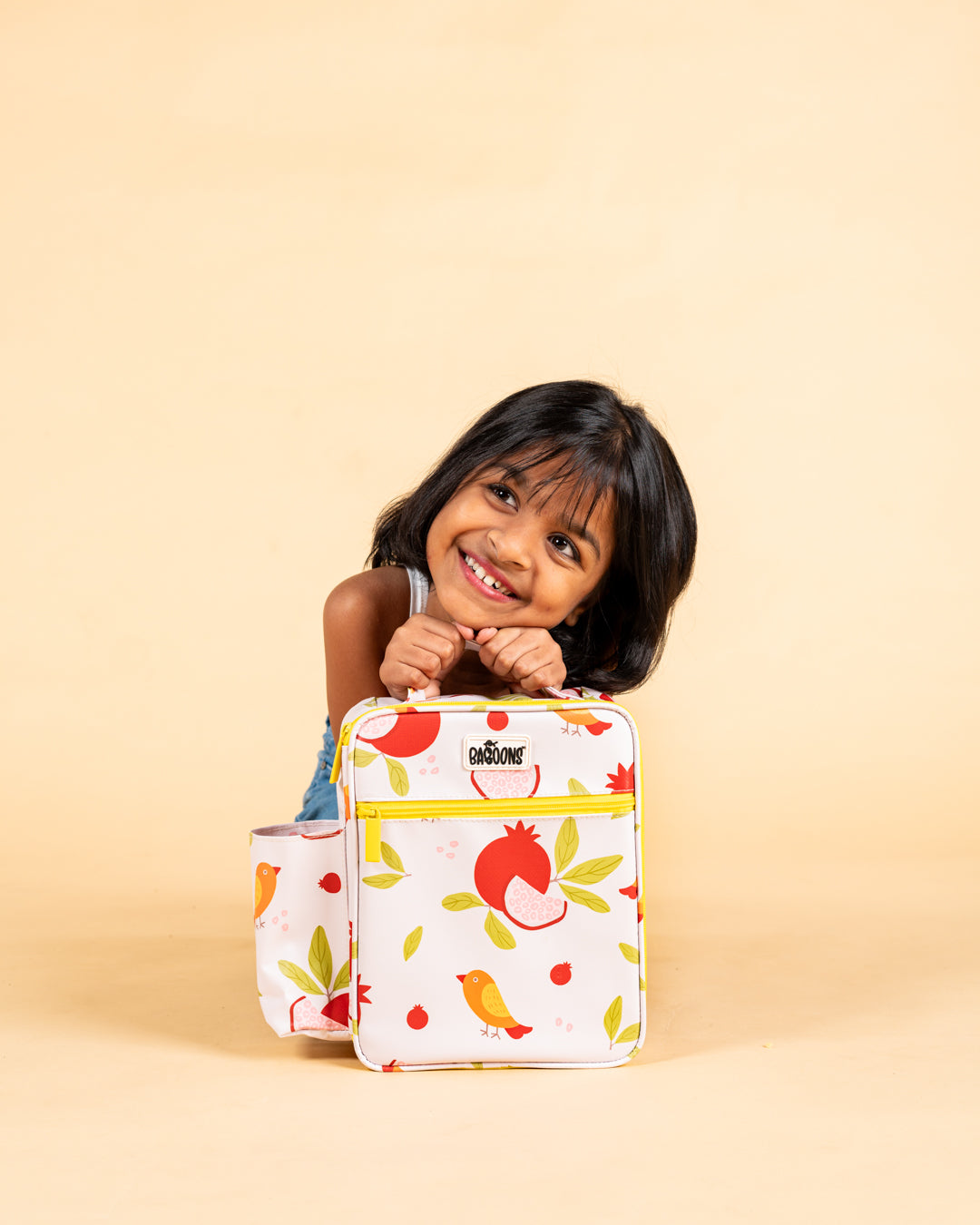 Smiling girl holding Baboons insulated kids lunch bag - pomegranate design, durable, water-resistant, perfect for bento boxes and snacks, available in India