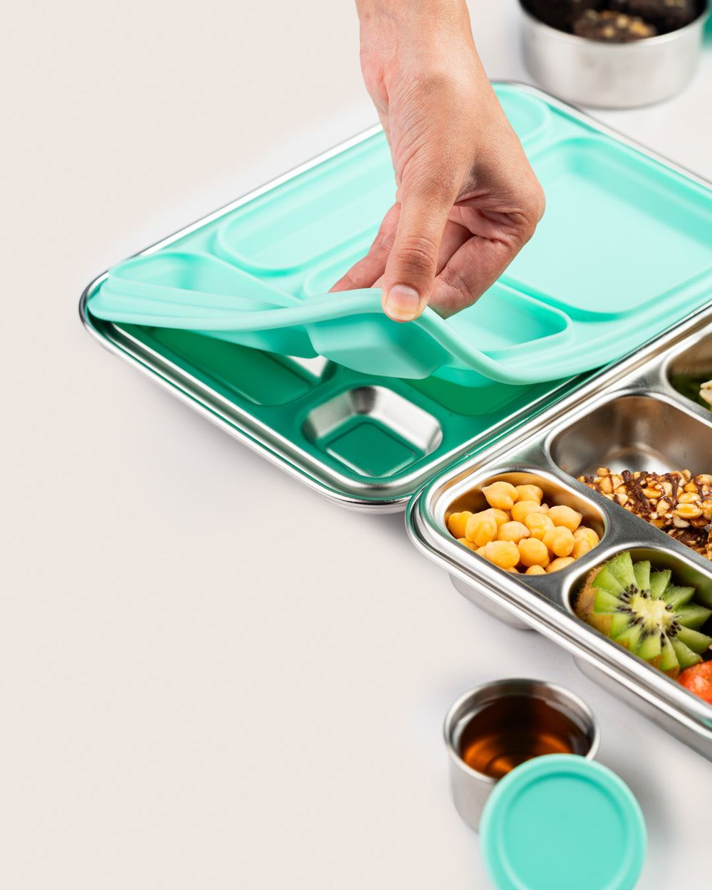 Aqua leakproof stainless-steel lunchbox with removable silicone liner being demonstrated by hand.