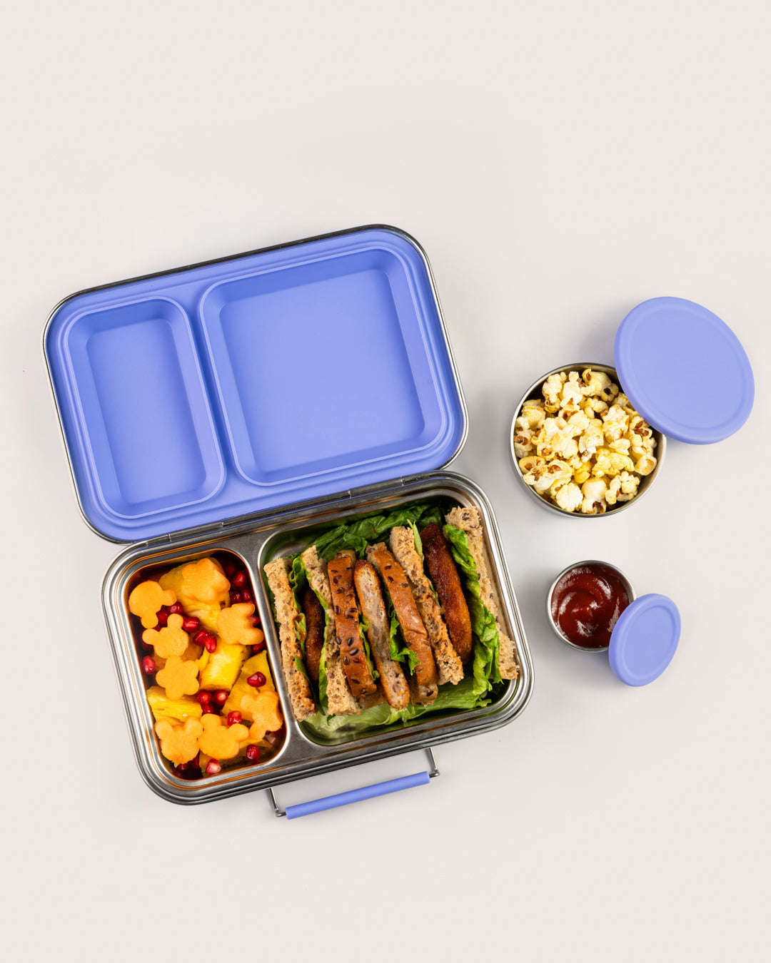 Best purple stainless-steel leakproof lunchbox in India with two compartments, containing healthy sandwich, fruit salad, popcorn and ketchup dip, perfect for kids and adults, eco-friendly and durable.