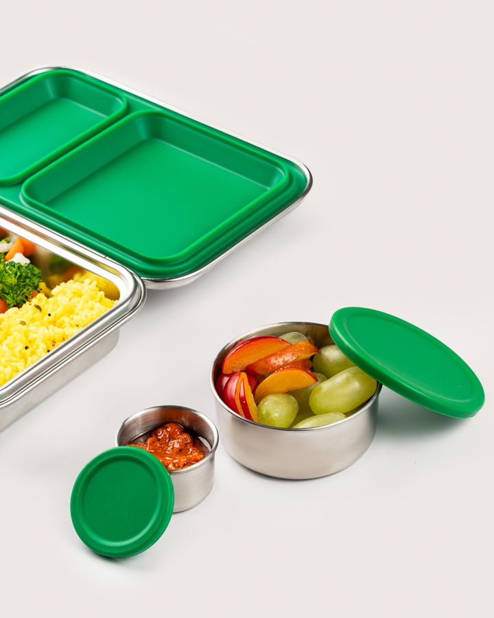 Stainless steel snack container set with green silicone lids, featuring a large container filled with fruits and a small container with dip, perfect for healthy snacking in India