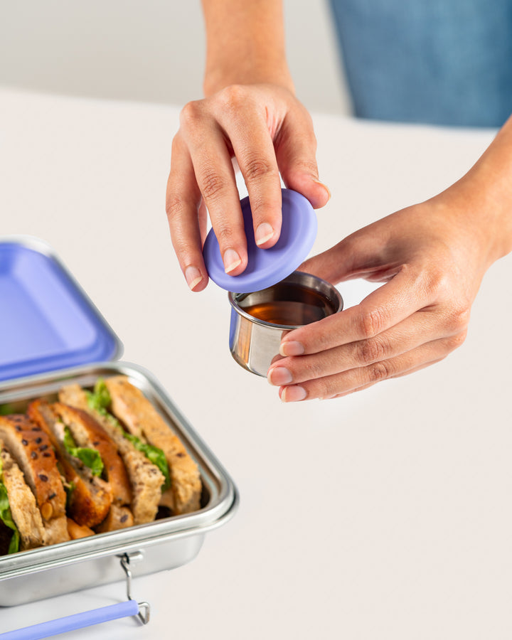 Hand closing a silicone lid on a leakproof purple snack container set with sauce, perfect for storing sandwiches and snacks in India