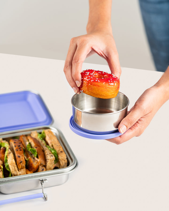 Hand placing a donut into a leakproof purple snack container set with silicone lids, perfect for sandwiches and snacks in India