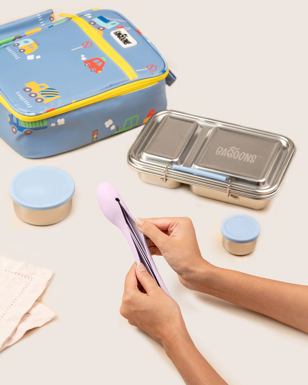 Mom packing reusable stainless steel cutlery set into silicone carry pouch next to eco-friendly school lunchbox and car lunchbag India Baboons.